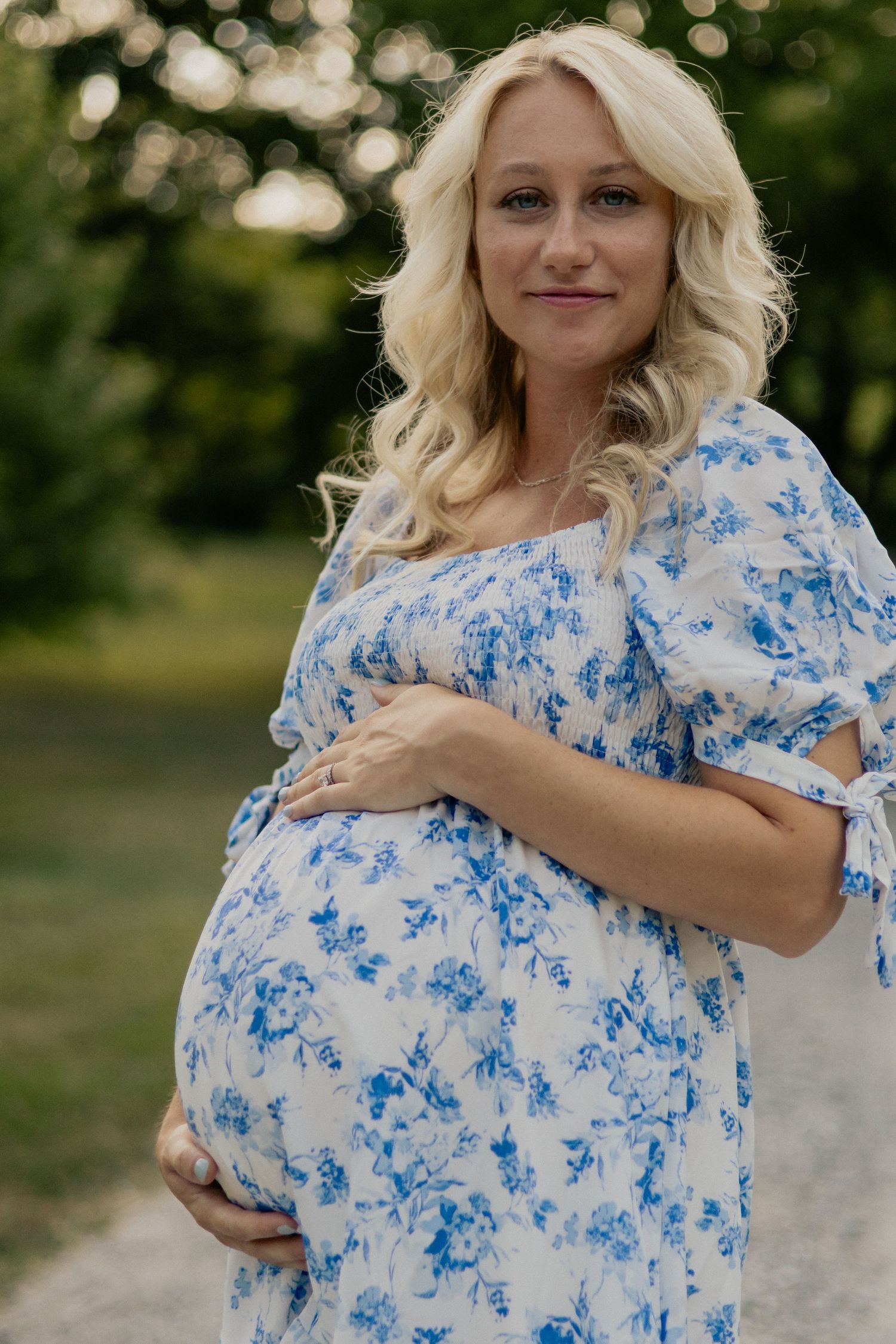 A maternity portrait showcasing a blue and white floral dress against a natural backdrop.