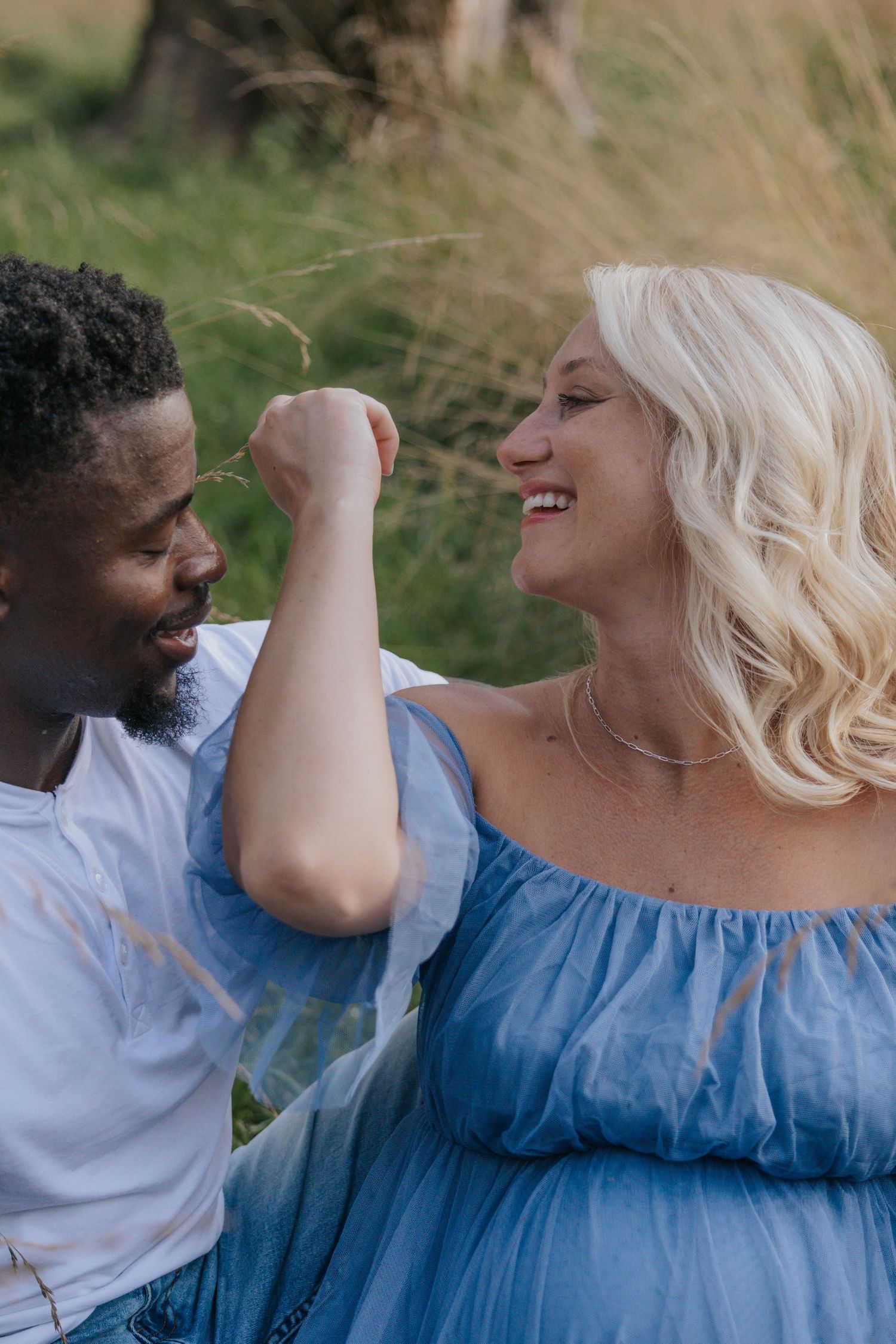 Joyful couple share a laugh together during outdoor maternity photoshoot.