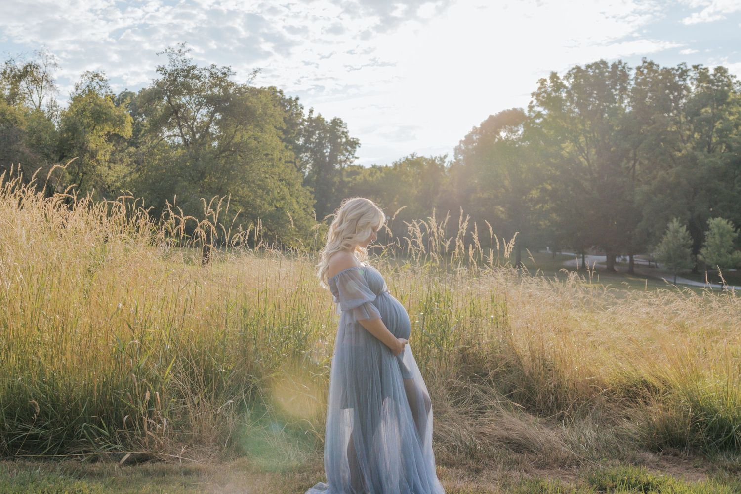 A dreamy maternity photo in a sunlit field of tall golden grass.