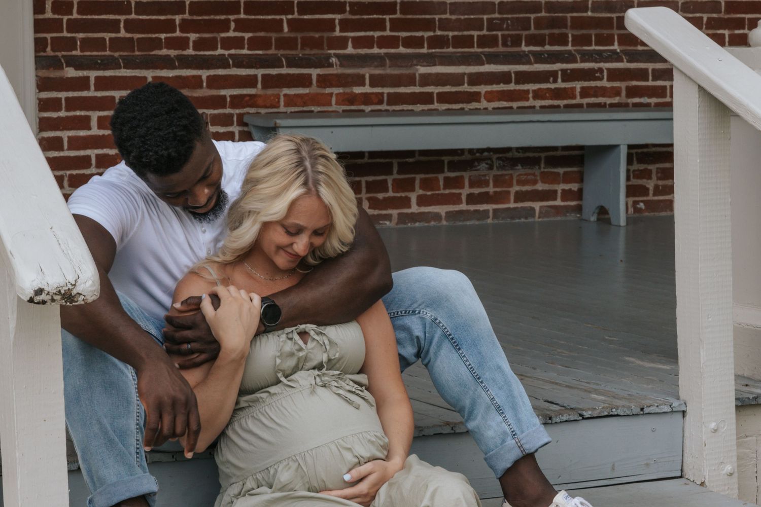 Couple sharing intimate moment on outdoor porch steps during maternity photoshoot.