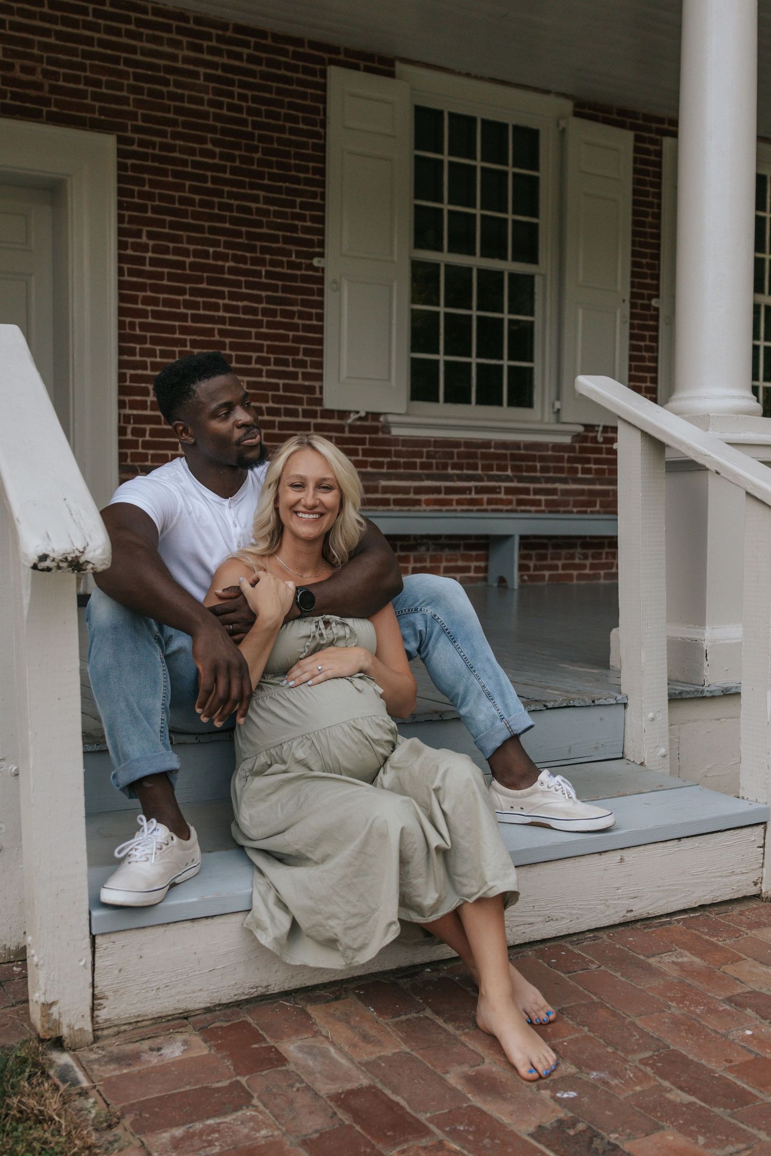 Couple relaxing together on brick porch steps during casual maternity photo session.