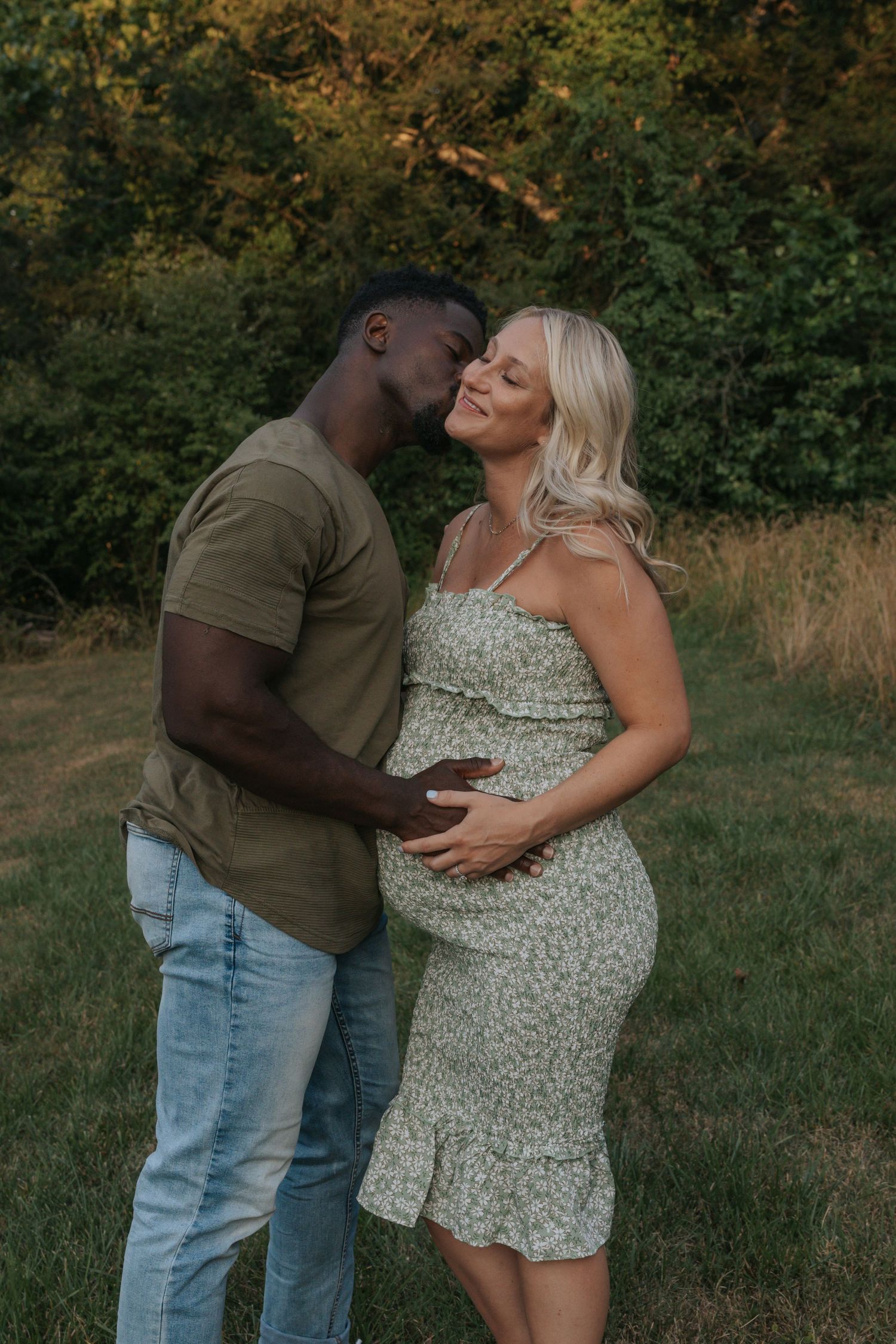 A tender maternity moment captured in a natural outdoor setting at golden hour.