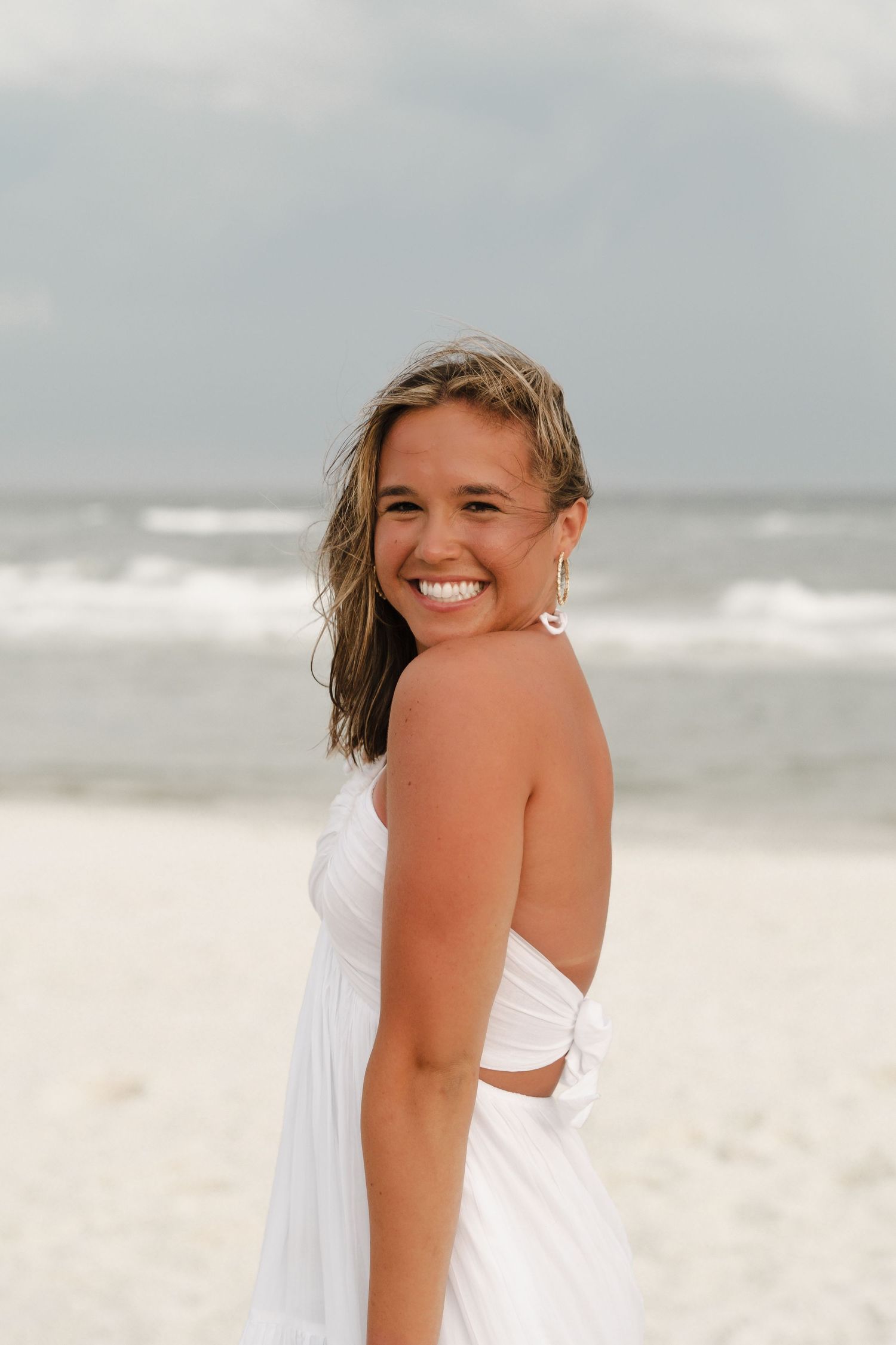 Woman in white dress posing on beach with ocean waves in background.