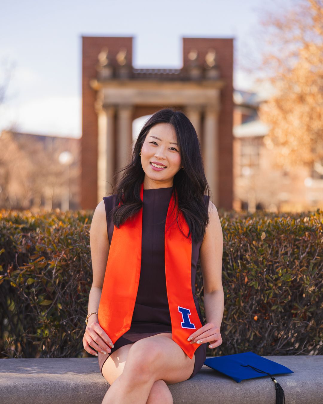 Graduating student sitting on concrete with her cap in front of Hallene Gateway at the University of Illinois