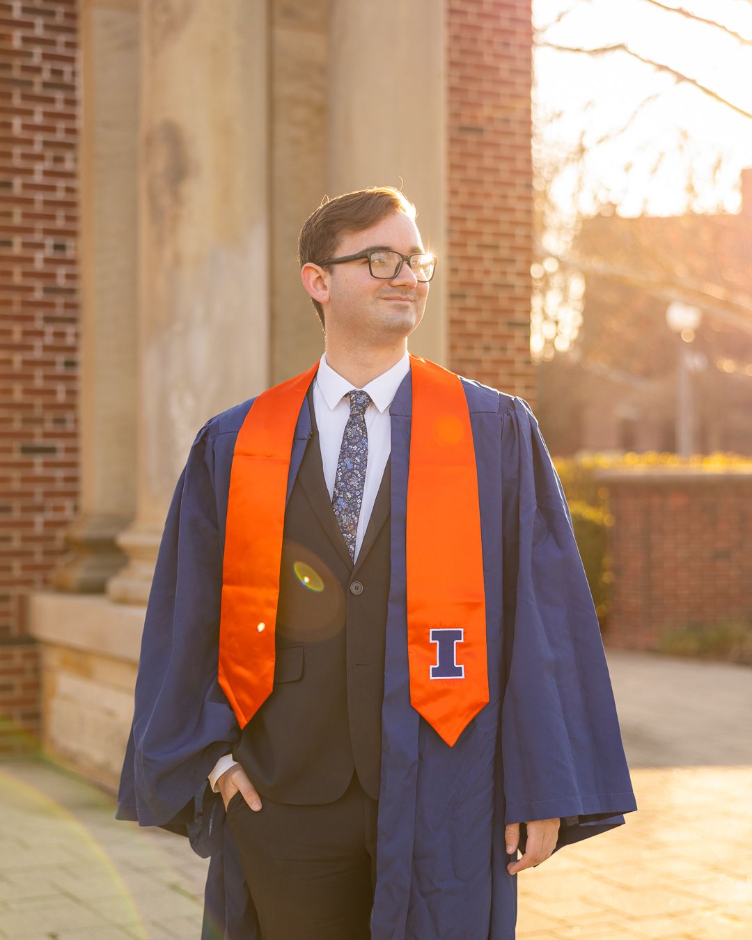 Guy with glasses looking off into the distance with a UIUC graduation stole on
