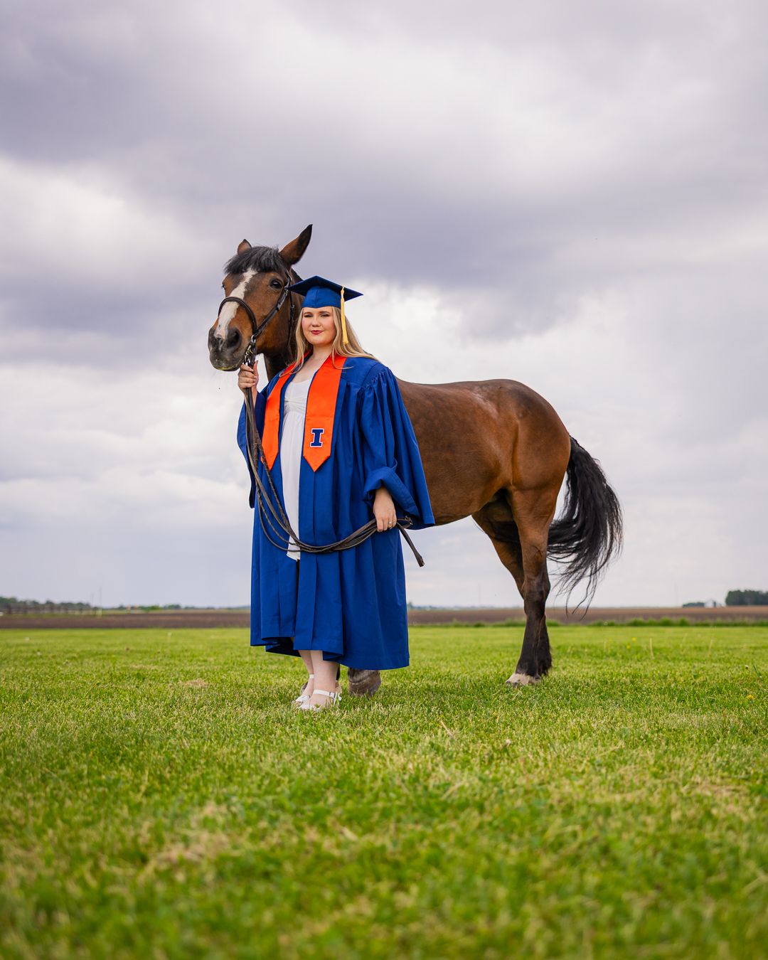 Graduating student at UIUC with cap and gown with her horse in a field