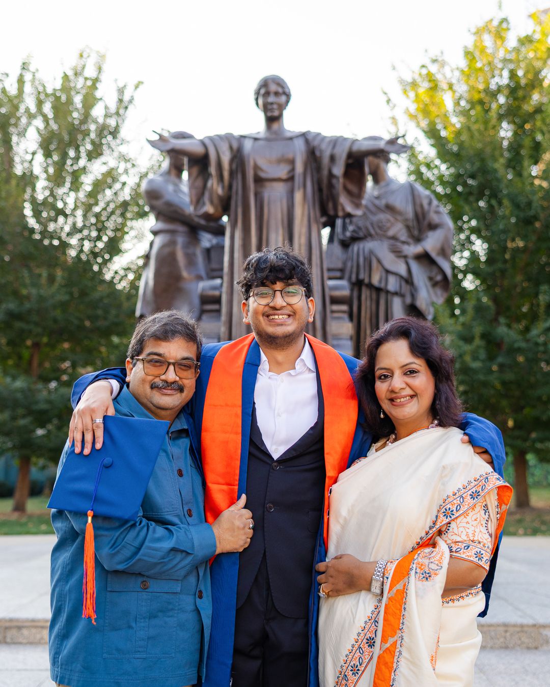 Graduating student's family smiling with graduation attire in front of U. of I. Alma Mater