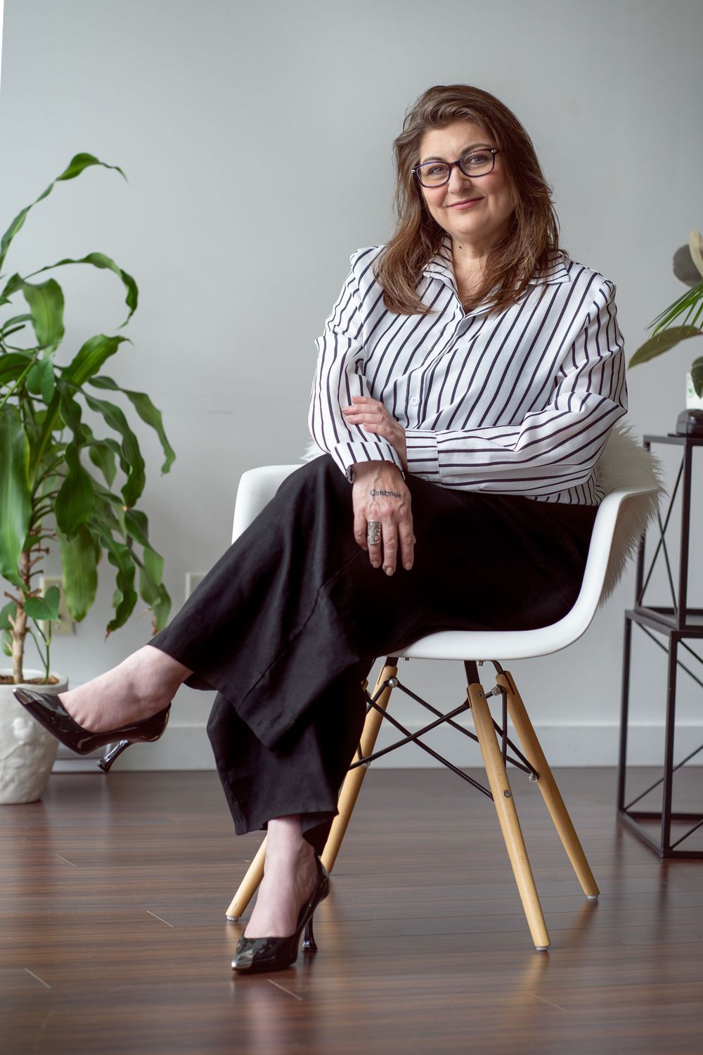 Business casual portraits in striped shirt and black pants seated in modern white chair.