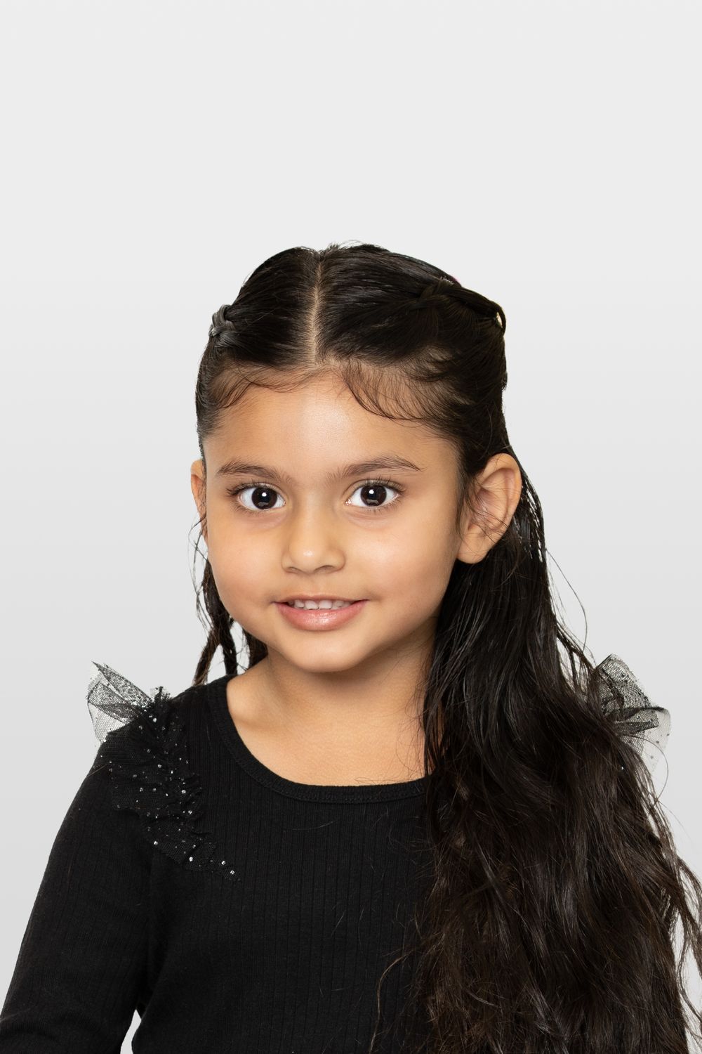 A young child with long dark hair wearing a black top smiles warmly at the camera.