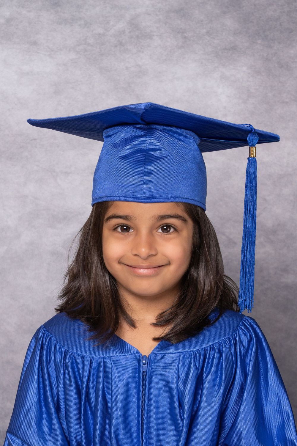 Graduate portrait series in royal blue cap and gown against grey background.