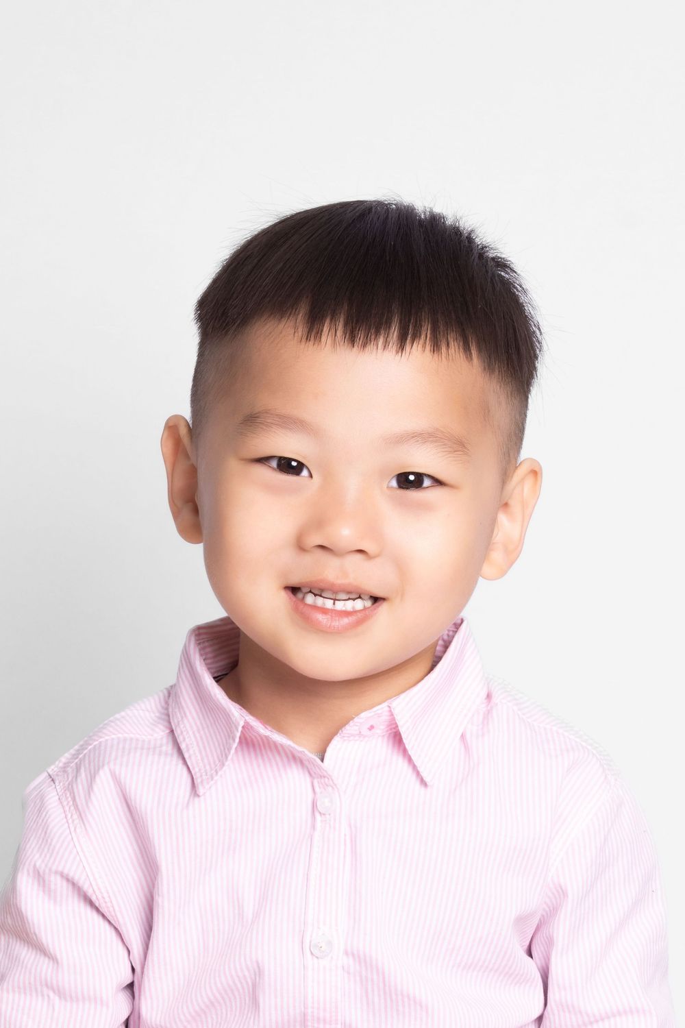 Child in pink striped shirt smiles for portrait against white background.