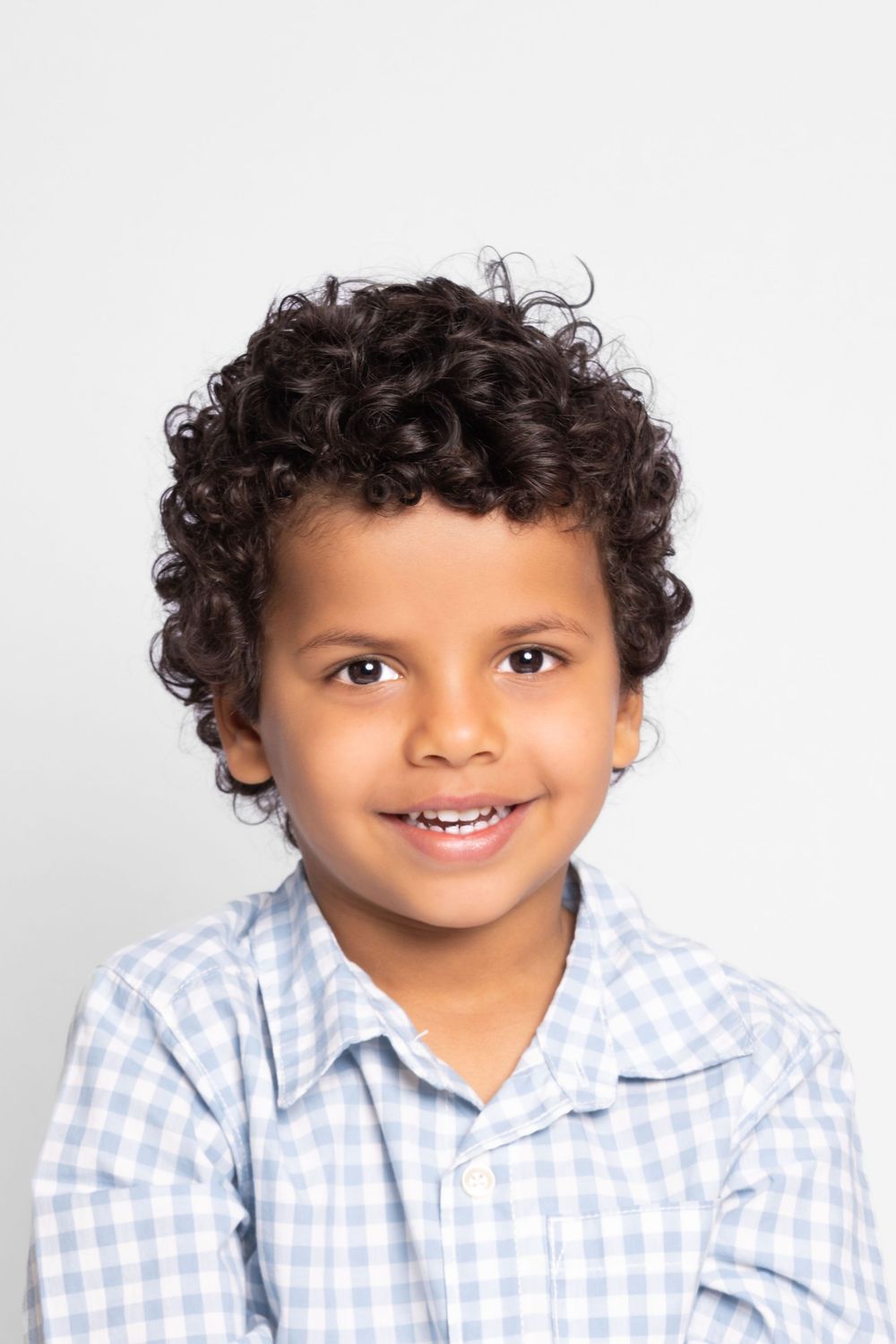 Young child wearing a light blue checkered shirt smiles in a series of four similar poses against a white background.