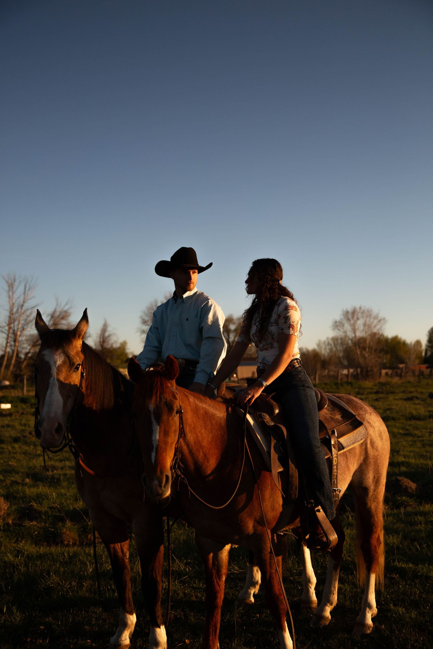 Row of horses and riders silhouetted against sunset sky in rural setting.