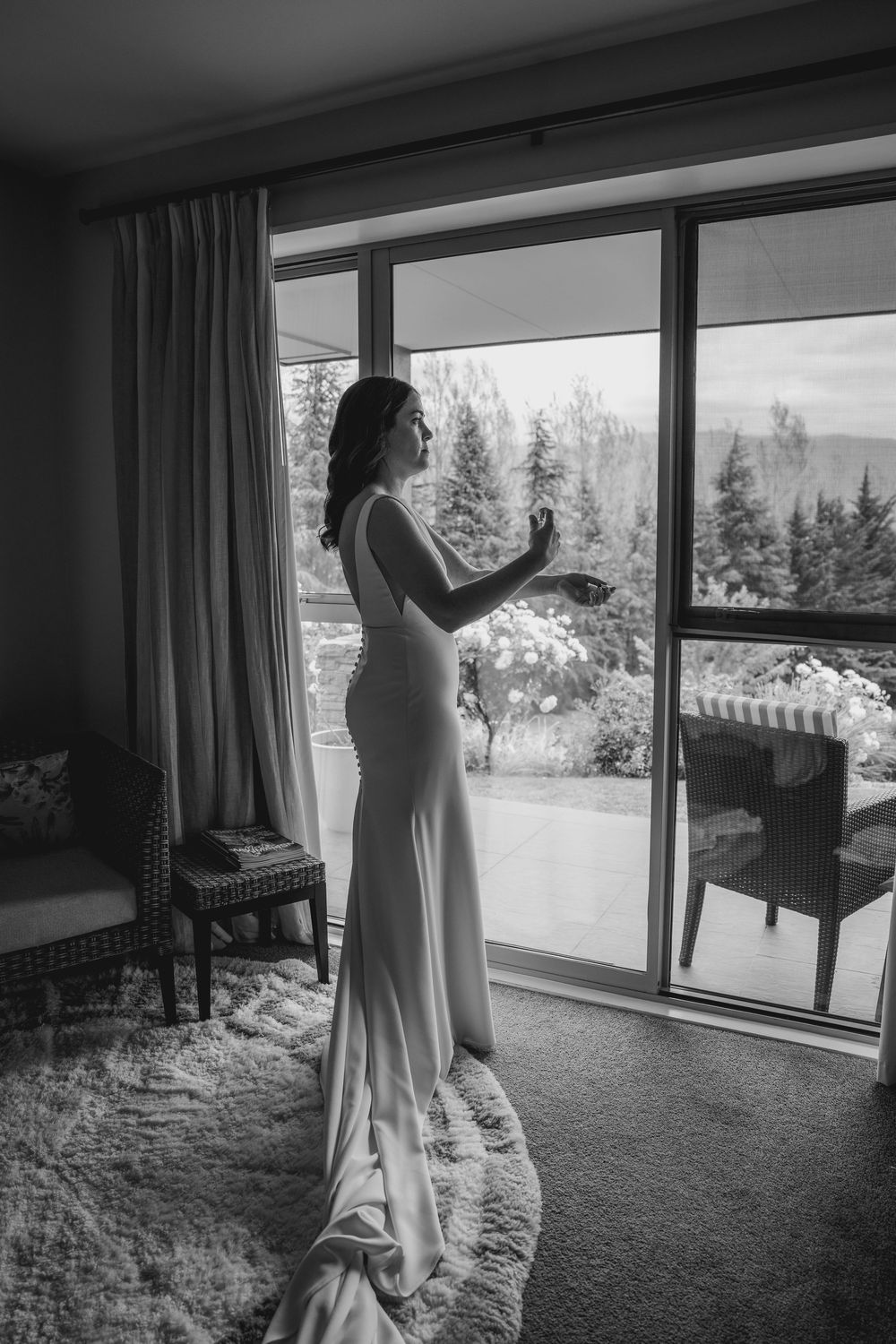 Bride spraying perfume on in front of a window before her wedding
