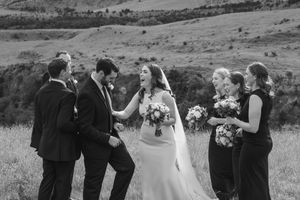 Bridal party laughing and dancing in a paddock black and white