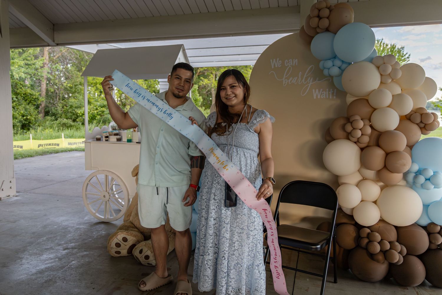 A festive baby shower celebration with a balloon arch featuring beige and light blue colors in an outdoor covered patio area.
