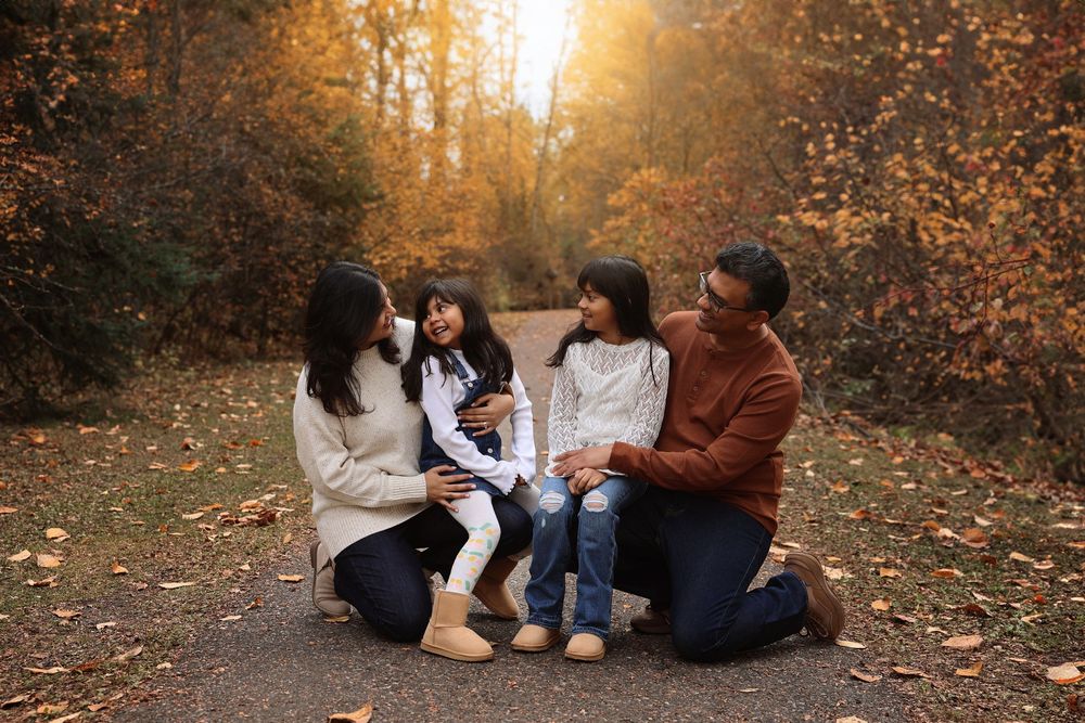 Group sitting together on fallen leaves along a forest path during golden hour.