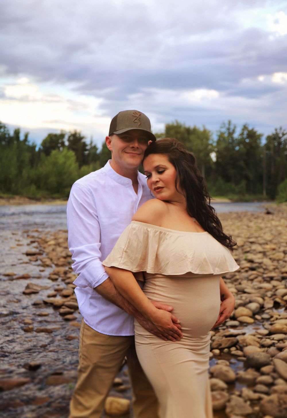 A couple embraces by a river during sunset for their maternity photos.