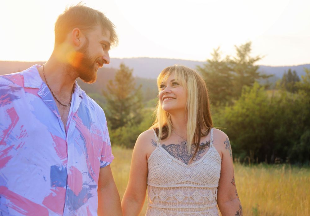 Romantic couple embraces in a sunlit meadow during golden hour with mountains in the background.