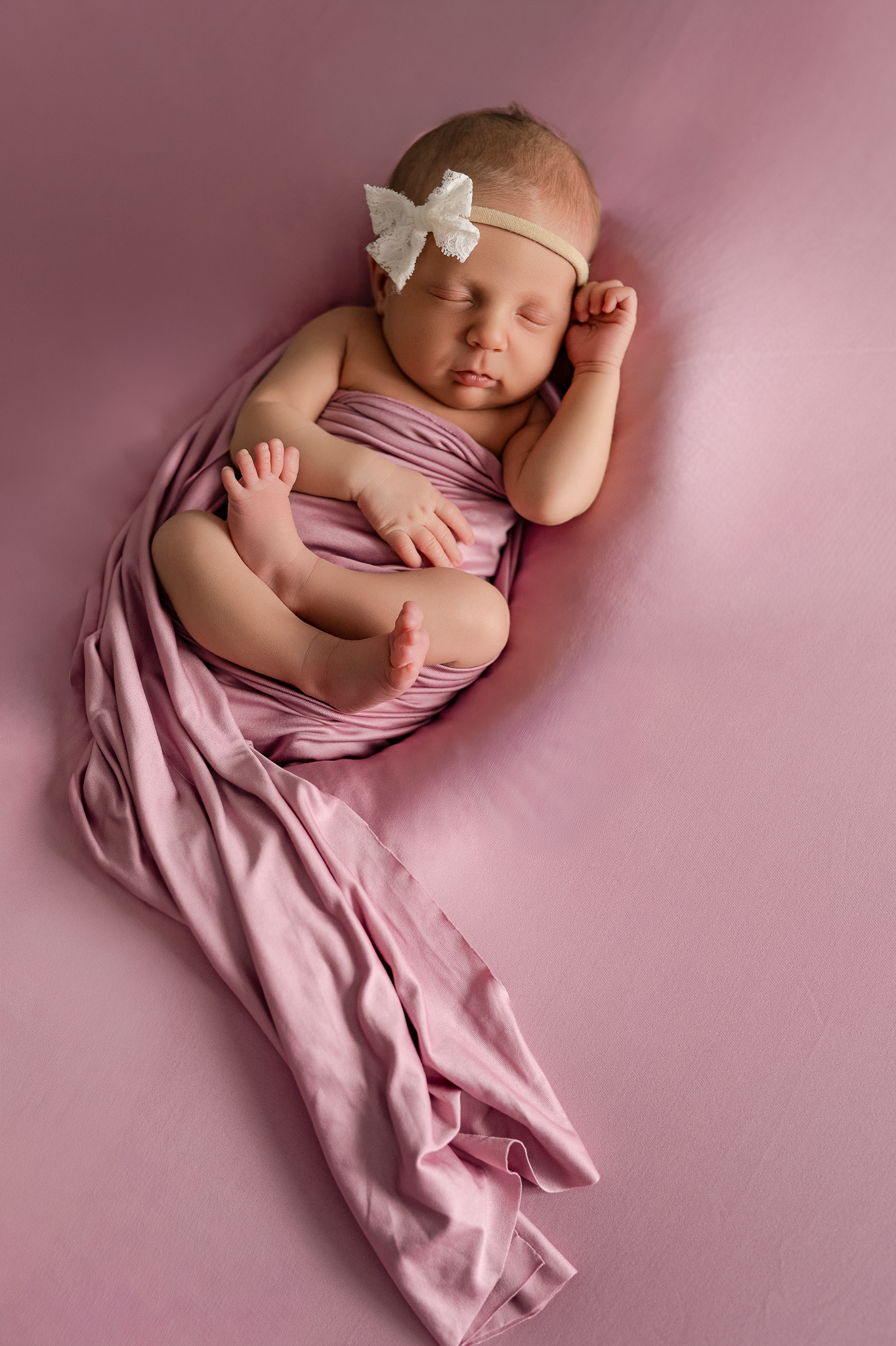 Smiling newborn baby wearing pink wrap and white bow headband.