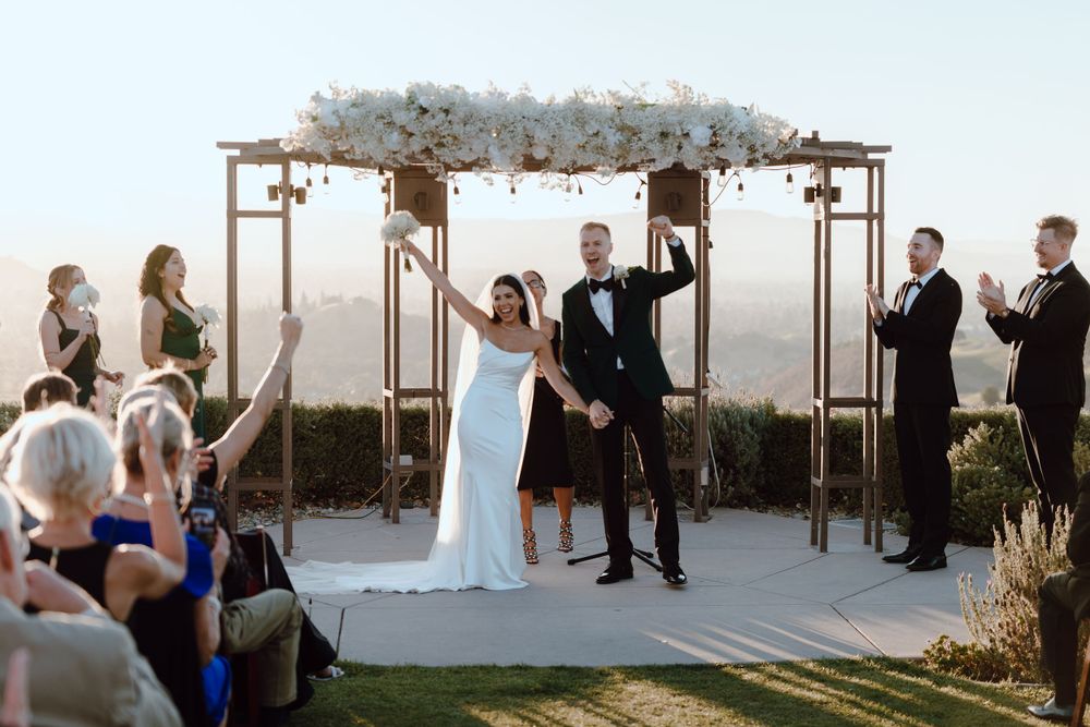 Wedding ceremony under a floral arch at sunset with mountain views.