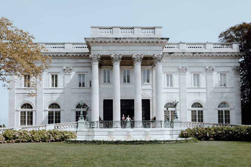 Panoramic exterior view of a grand white neoclassical mansion with ornate columns and architectural details.
