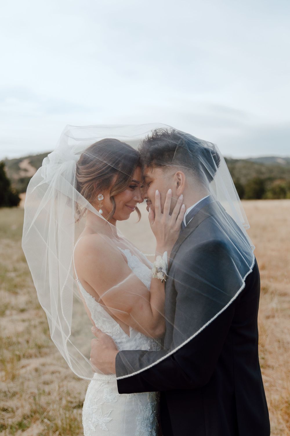Romantic sunset moment with couple embracing under flowing white veil.