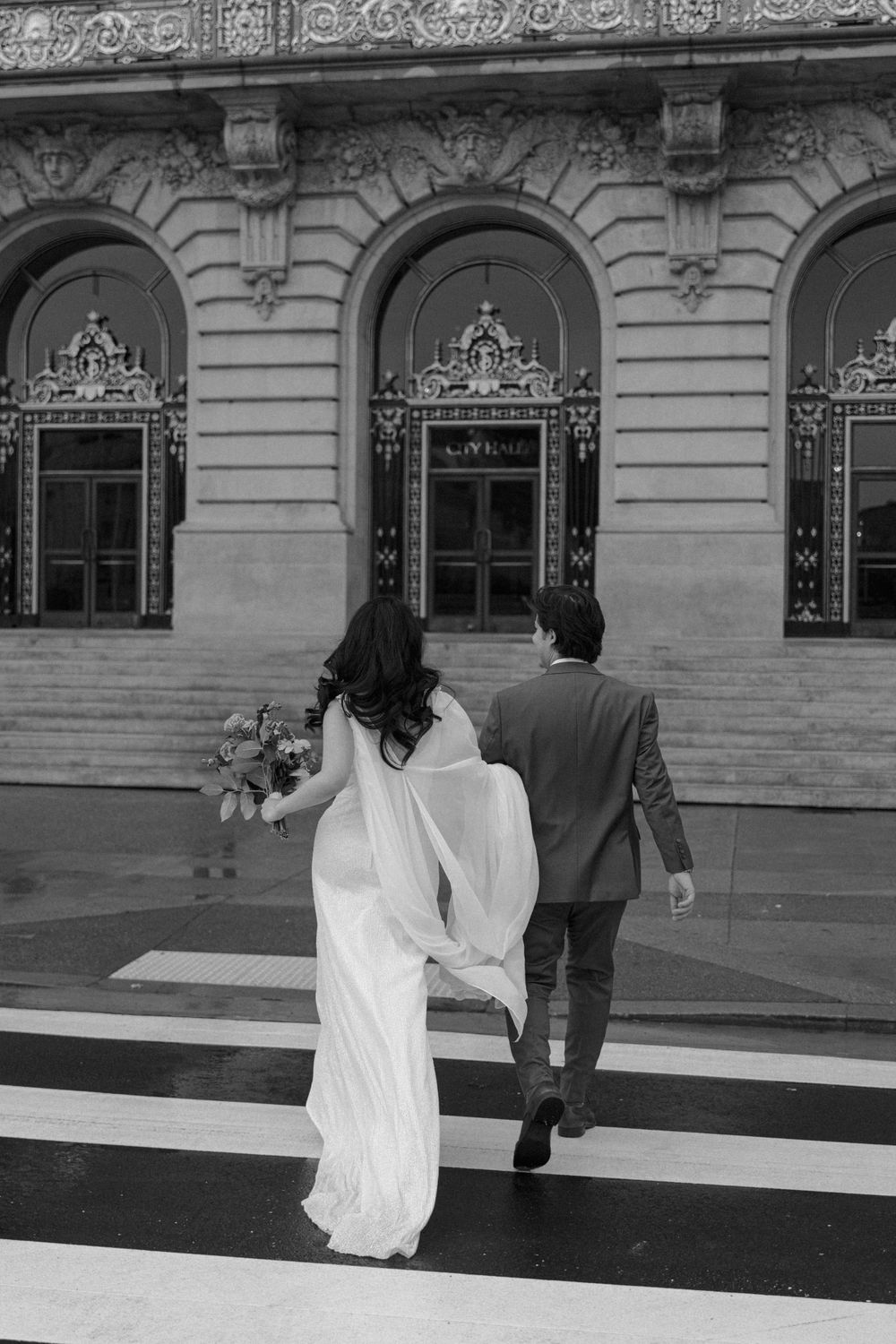 A couple in wedding attire walking up steps of a historic building with ornate architecture.