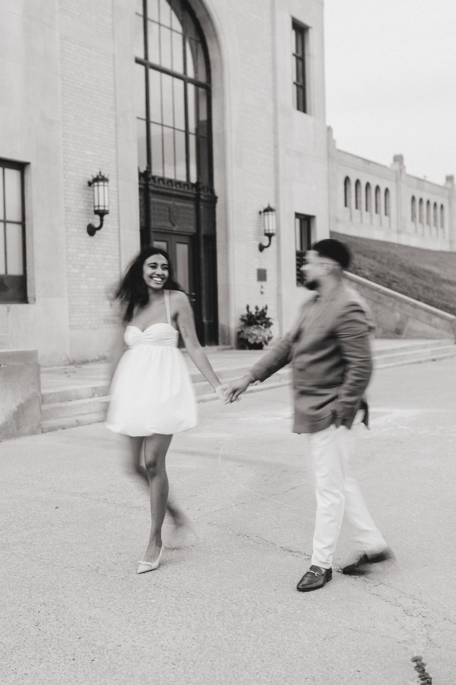 A playful black and white photo of a couple dancing outside a historic building entrance. Indian Wedding Photography Toronto GTA