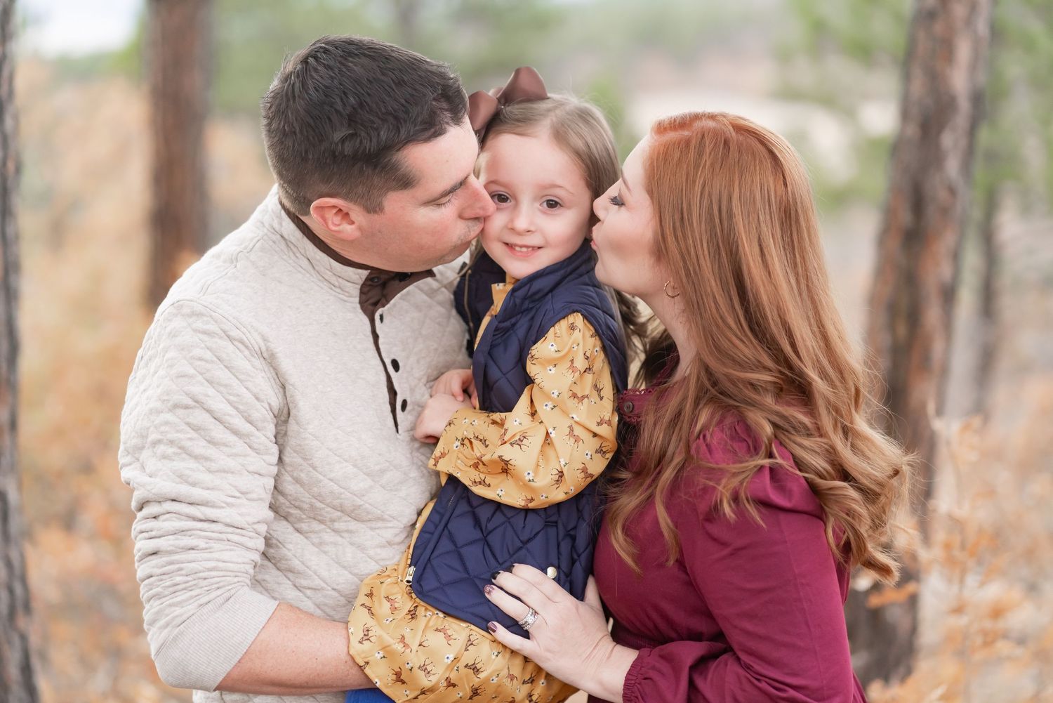 Parents share tender moment with their young child in autumn forest setting.