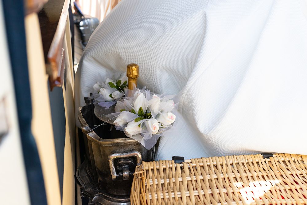 Champagne bottle with white flowers in a wicker basket on a luxury boat seat.