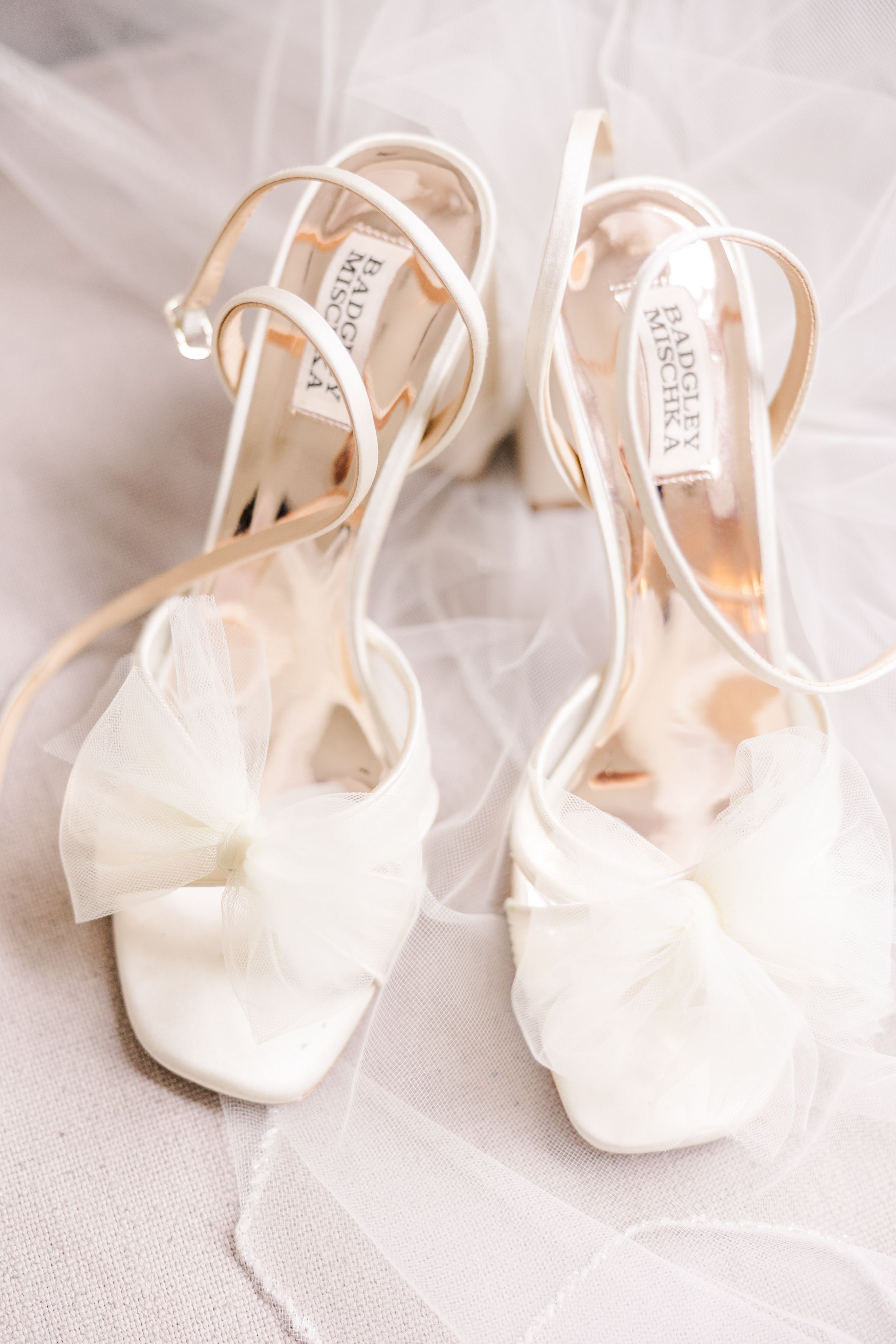 Elegant white bridal heels with straps displayed on light fabric.