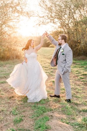 Newlyweds dancing together in a field during golden hour.