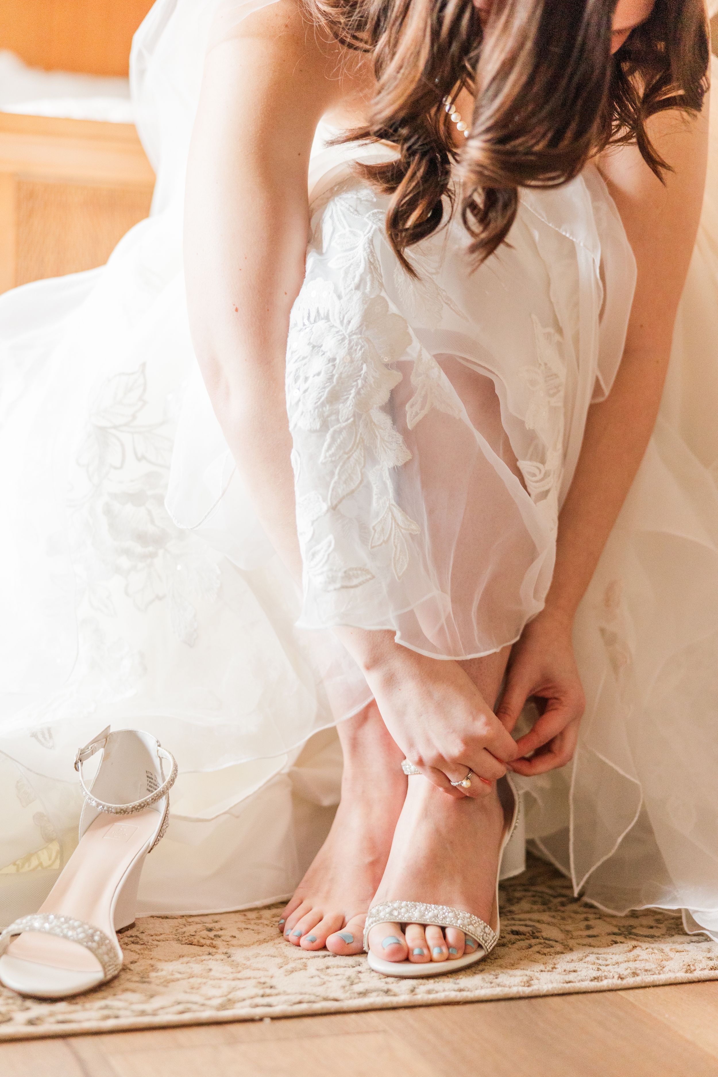 Close-up of bride adjusting her white sandal while wearing flowing wedding dress.