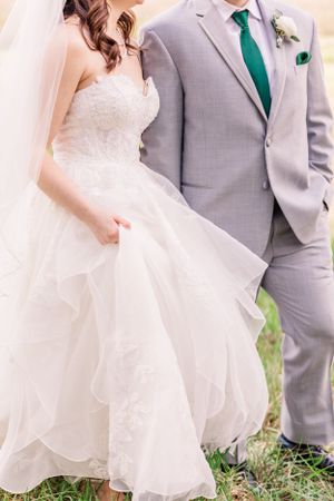 Wedding couple in grey suit and white gown stand together showing formal attire details.