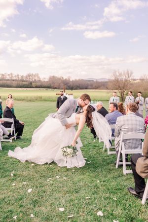 Joyful couple sharing romantic dip kiss during outdoor wedding ceremony.