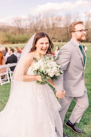 Happy newlyweds walk hand in hand down aisle after outdoor ceremony.