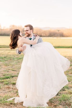 Groom lifts bride in flowing white dress during sunset portrait session.