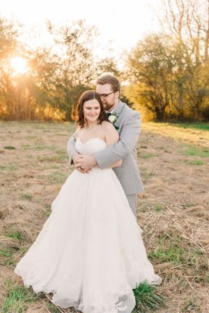 Romantic golden hour wedding portrait of a couple embracing in a field at sunset.