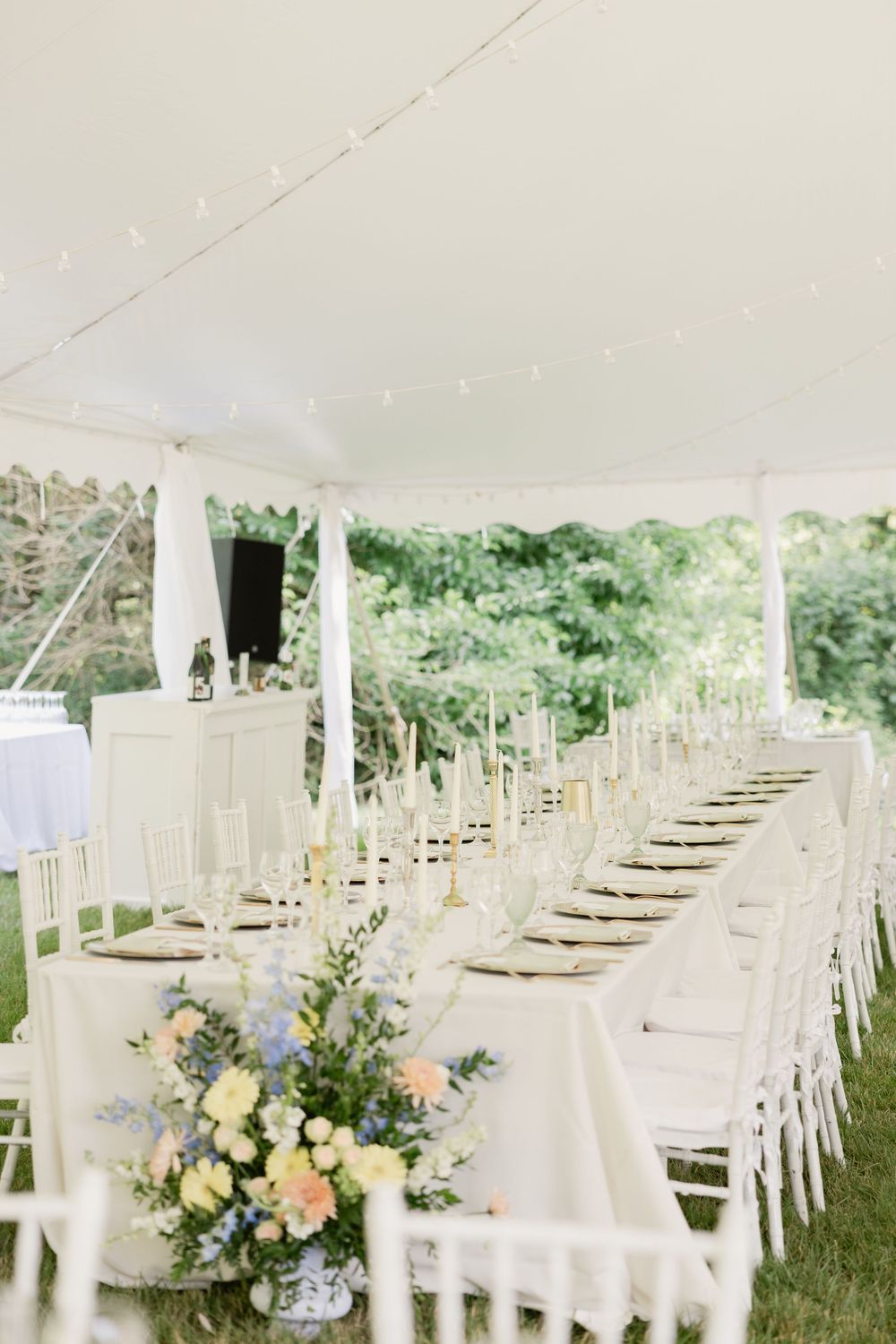 An elegant outdoor wedding reception setup with white chairs and tables under a tent, decorated with soft floral centerpieces.Cincinnati Wed
