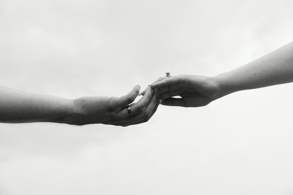 Two hands gently reaching and touching each other in a black and white photo symbolizing connection and support.