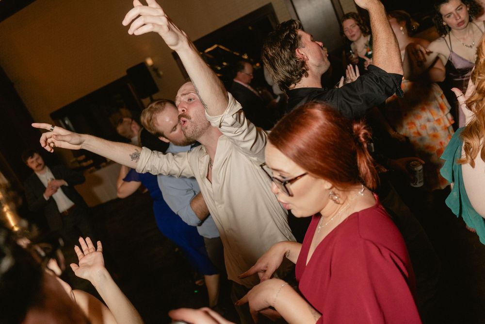 Energetic crowd dancing at a lively party event, with a red-haired woman in burgundy and man pointing upward.