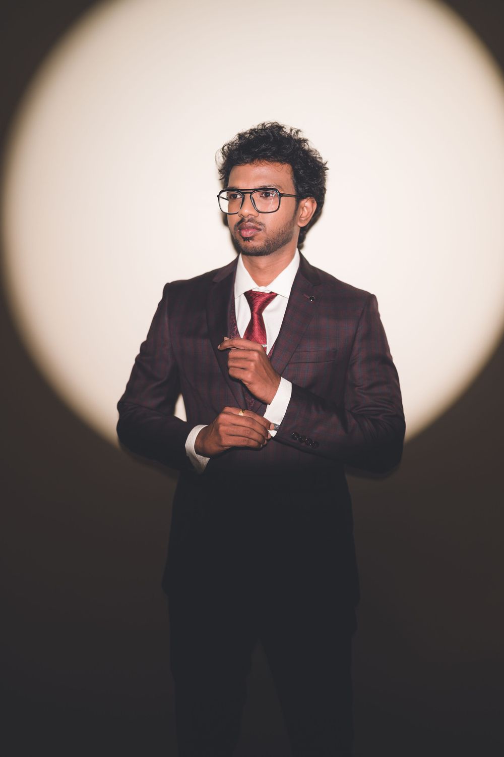 Professional portrait of a businessman in a maroon suit against a spotlit background.