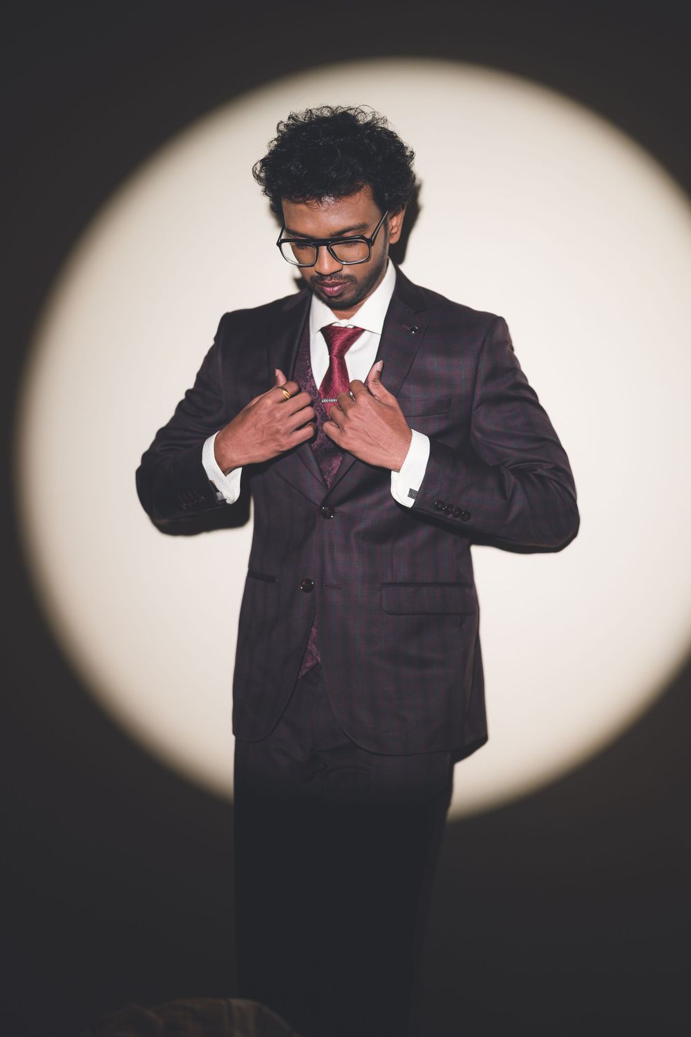 Stylish portrait of a man in a dark suit adjusting his tie in dramatic lighting.
