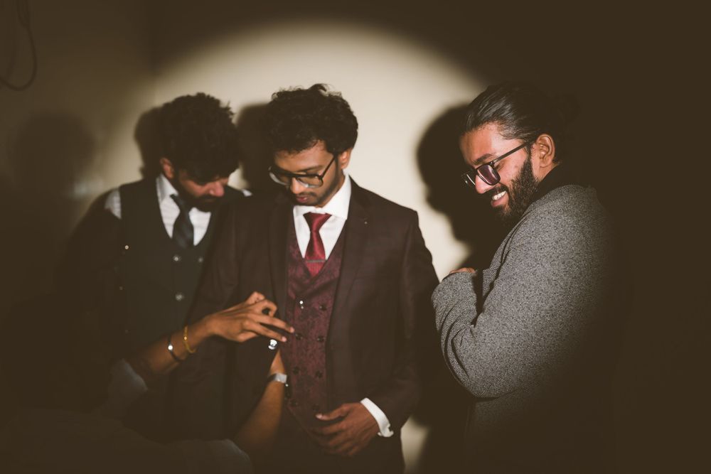 Three people in formal attire share an intimate moment laughing in dark moody lighting.