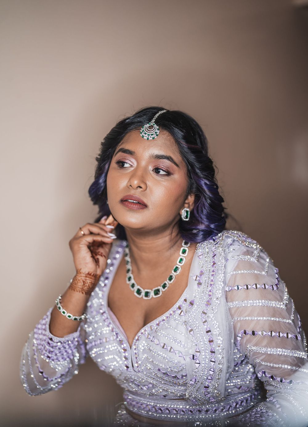 South Asian woman in lavender beaded gown poses elegantly with traditional jewelry and makeup.
