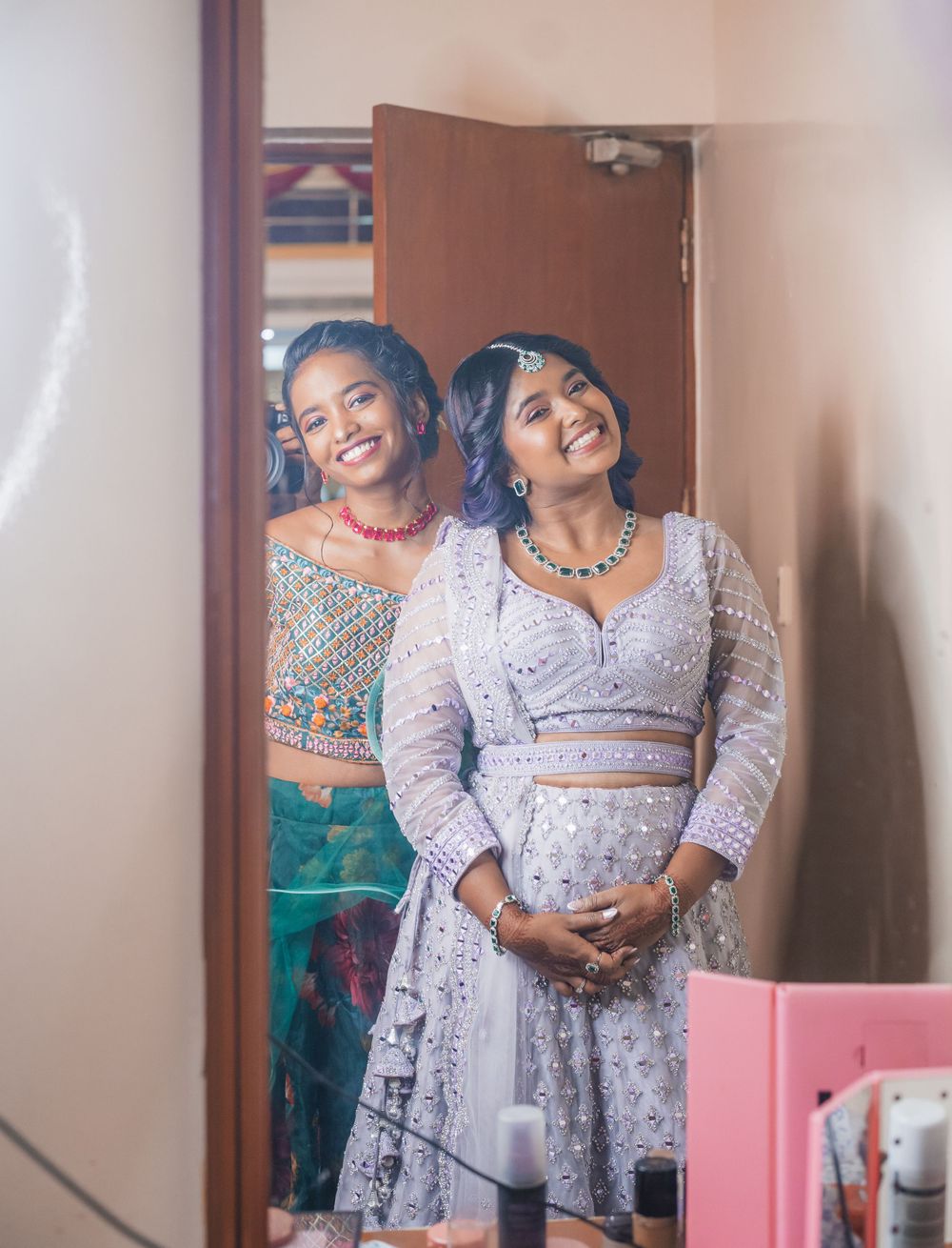 Two women in traditional Indian formal wear pose together joyfully in a dressing room.