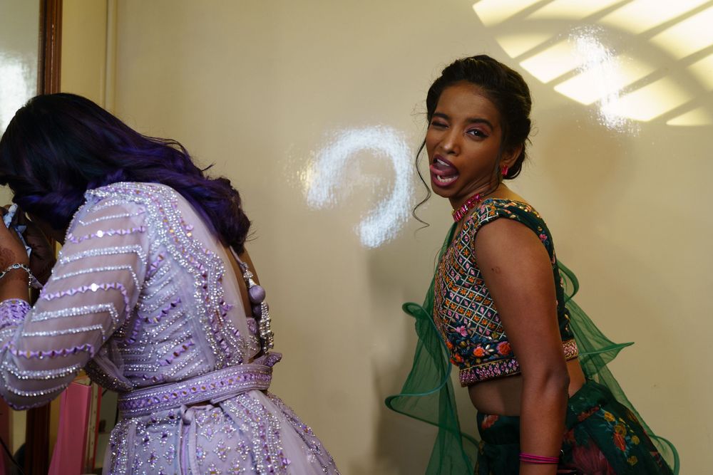 Women in traditional Indian formal wear share a candid moment in bright lighting.
