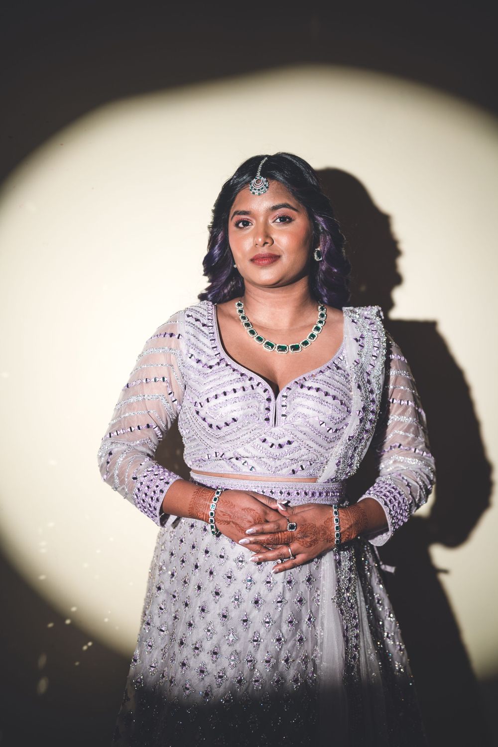 Dramatic portrait of woman in beaded white lehenga against circular spotlight background.