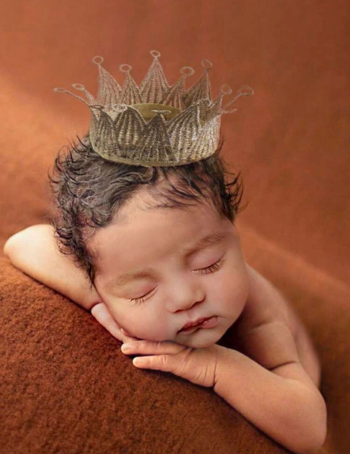 Sleeping newborn wearing a delicate silver crown on a brown textured backdrop.